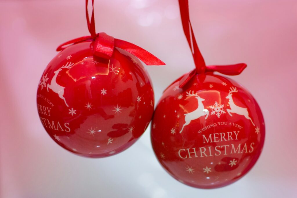 two red christmas ornaments hanging from a red ribbon